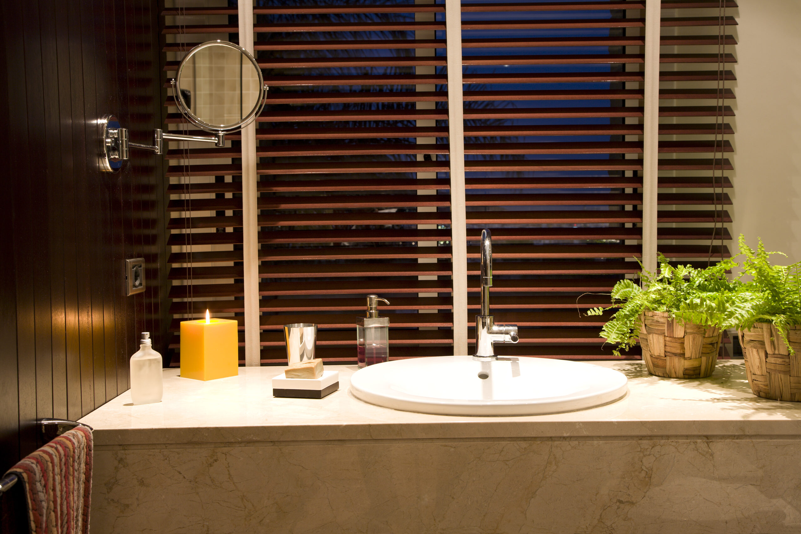 Porcelain  sink sorrounded by travertine marble with  dyed teakwood wall and blinds.