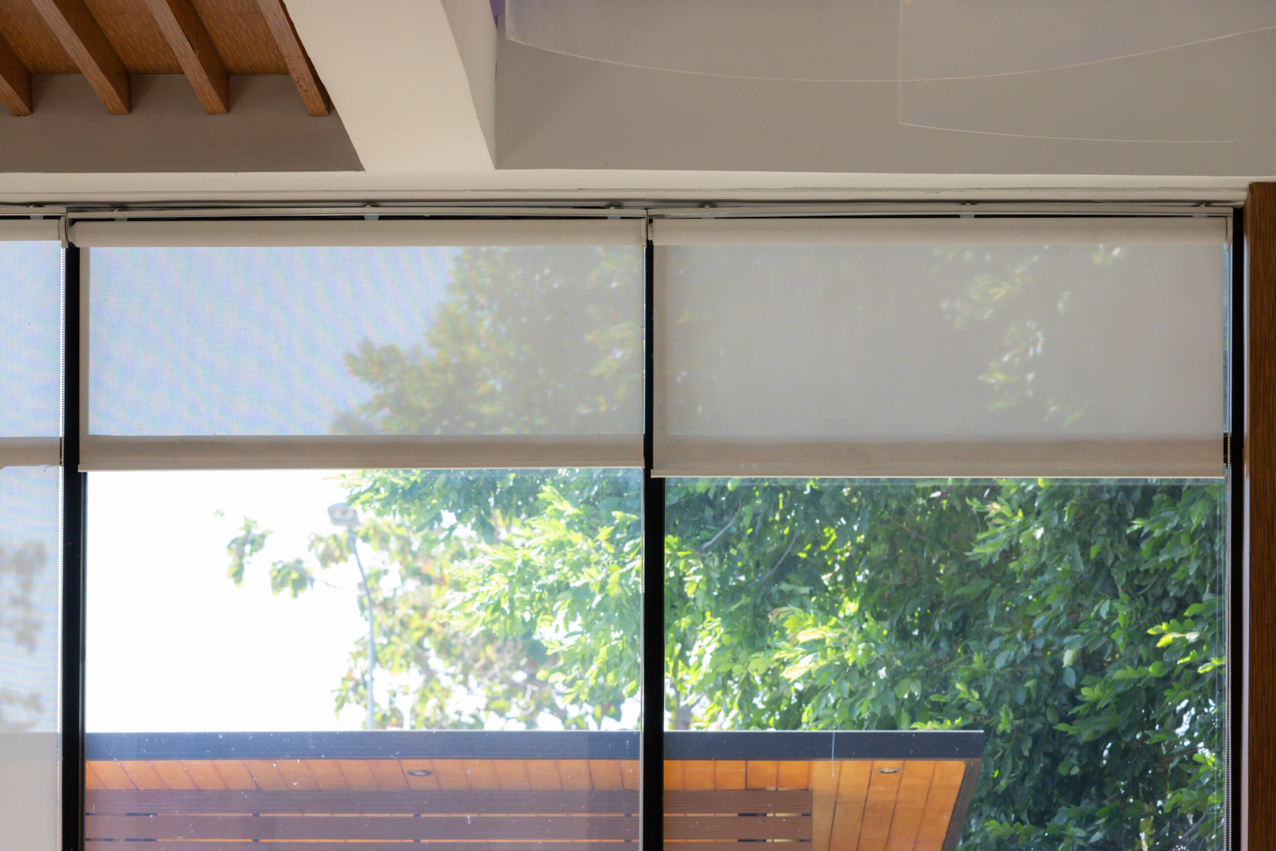 A large window with white blinds, allowing sunlight to stream in and illuminate the room. The room appears to be a living space, with a wooden floor and a wooden structure visible in the background