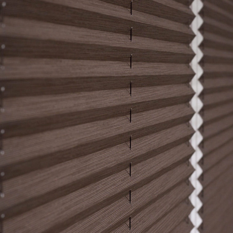 Pleated blinds close up on the window in the interior. Home blinds - cordless pleated modern shades on apartment windows. Brown color fabric.