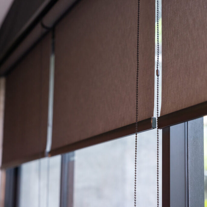 A window with a curtain that is hanging down. The curtain is brown and has a black chain