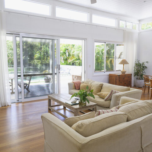View of interior with sofas, coffee table, dining table and chairs, sliding glass door for outside access and view of swimming pool and foliage.