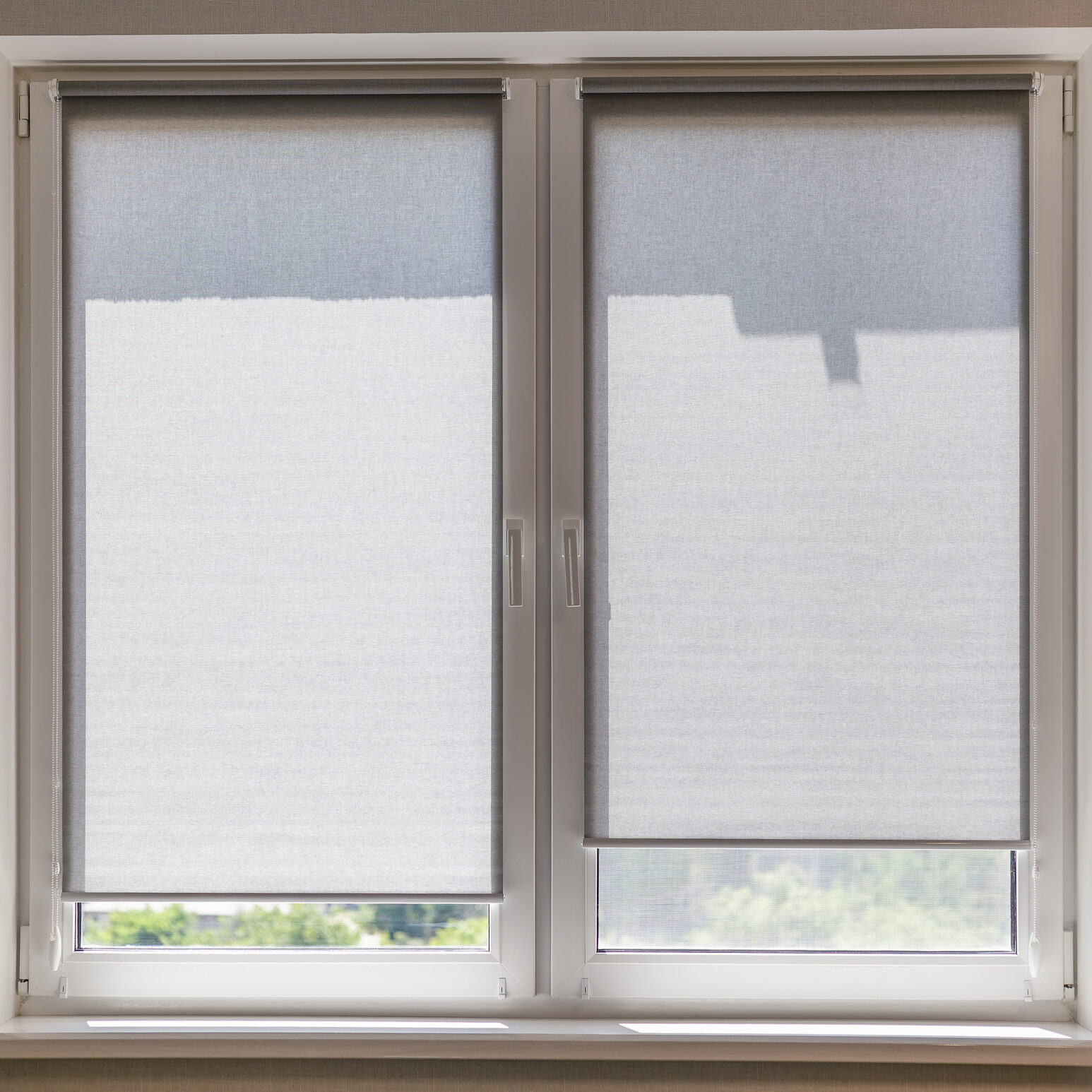 Gray roller blinds on the window close-up in the room on a sunny day. Small roller shades on the window sashes. Sunshade textured fabric with darkening ability.